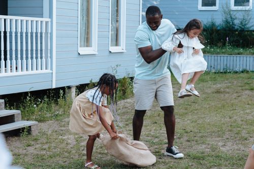 Free Father and daughters enjoying a playful day outdoors in the yard with smiles and laughter. Stock Photo