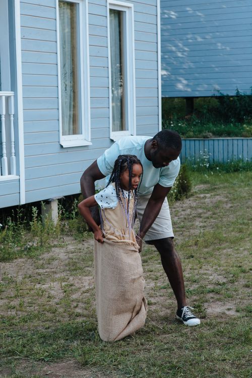 Free Father assisting his daughter in a backyard sack race, capturing a joyful family moment. Stock Photo
