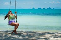 在一个阳光明媚的热带日子里，一名女子在碧绿的海水中荡着海滩秋千