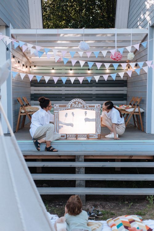 Free Adults and child enjoying a puppet show outdoors on a decorated deck. Stock Photo