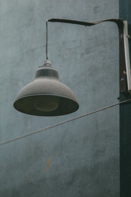 Free A rustic industrial wall lamp hangs outside against a weathered concrete wall, capturing an urban aesthetic. Stock Photo