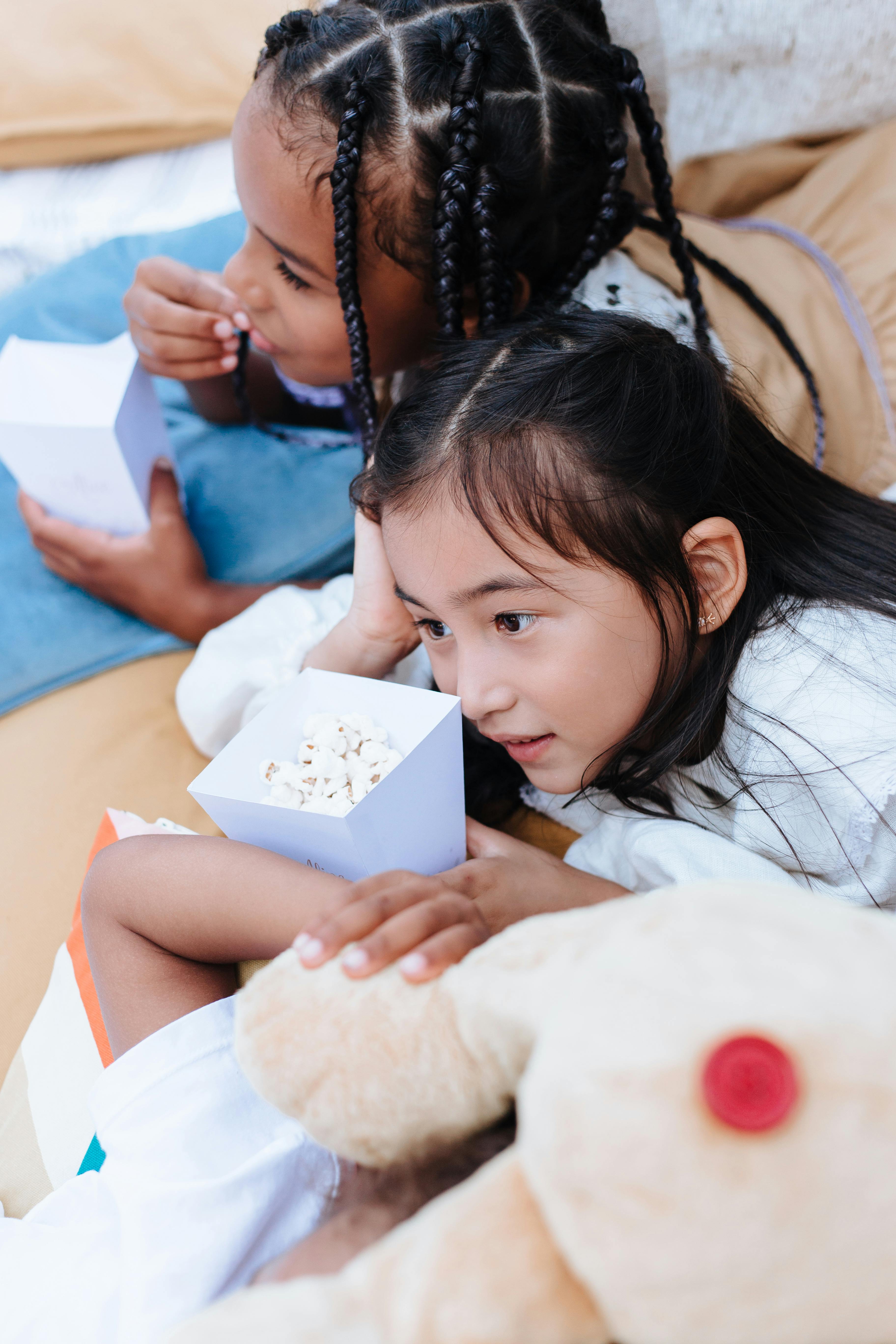 Two kids with popcorn boxes lie and enjoy leisure time indoors.