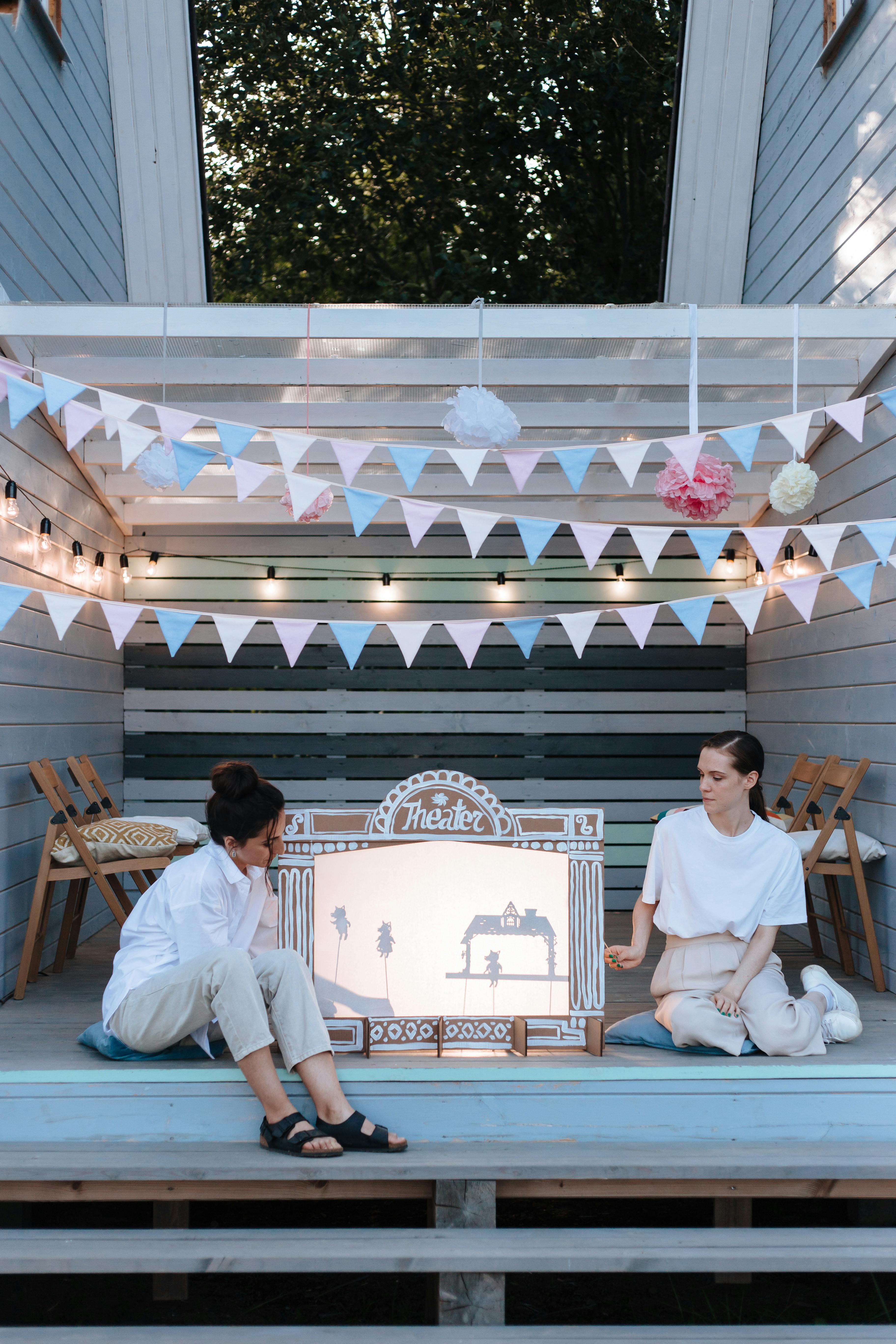 Free Two women enjoy a shadow puppet theater setup on a decorated deck. Stock Photo