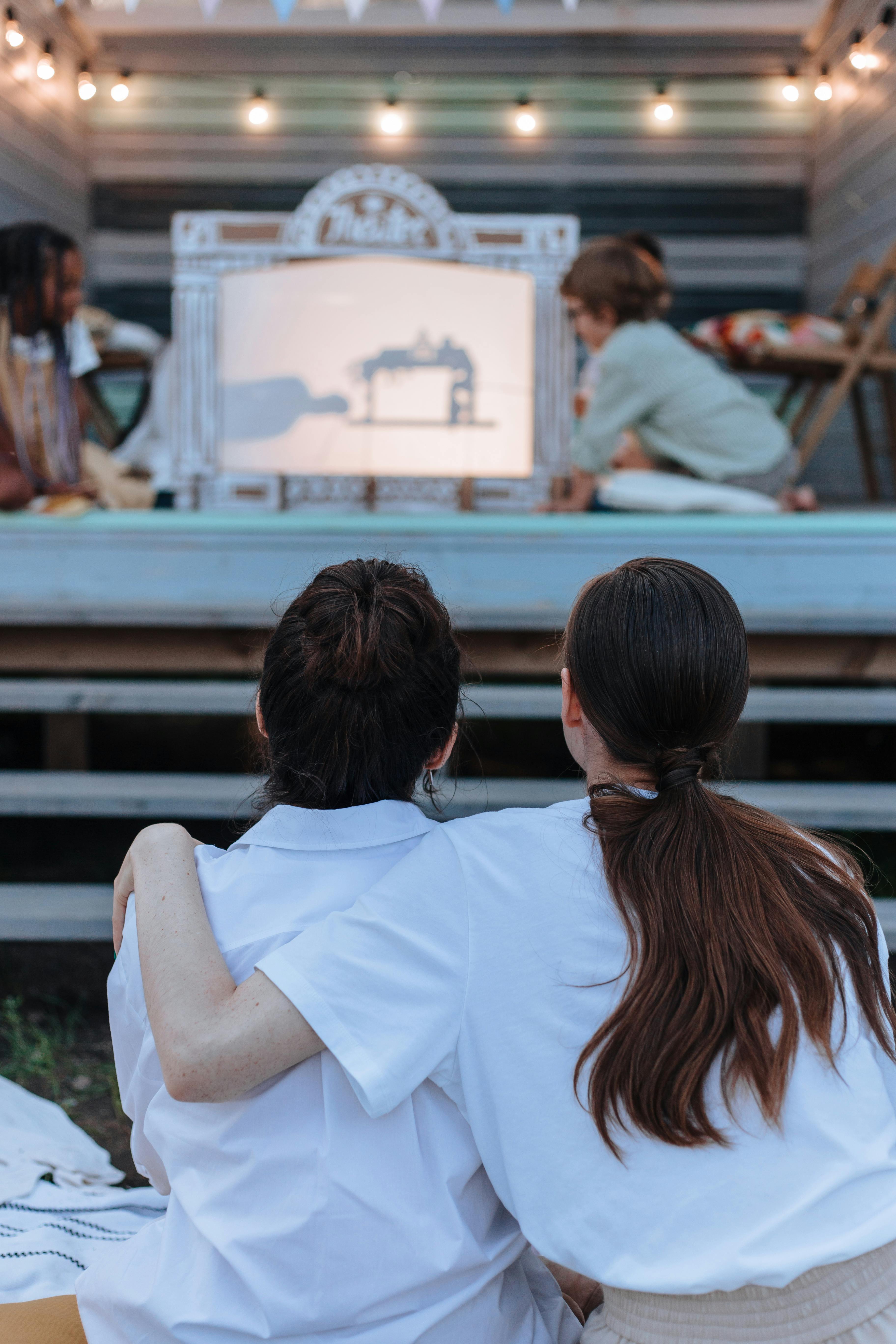 Free Two friends enjoy a shadow puppet show in a cozy backyard setting under string lights. Stock Photo