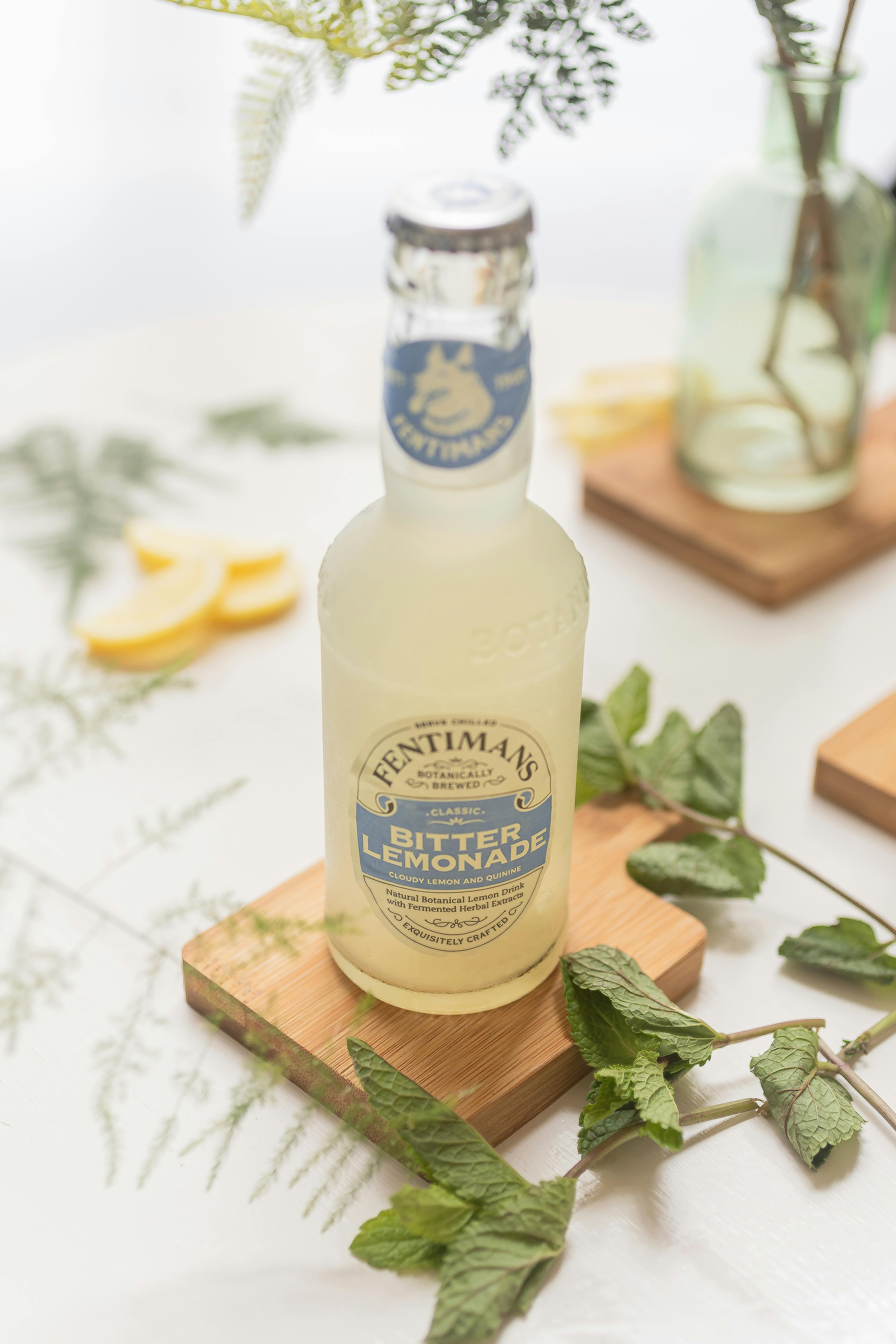 Close-up of Fentimans Bitter Lemonade bottle with mint leaves and lemon slices on wooden coasters.