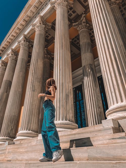 Free A woman poses gracefully beside towering architectural columns under a clear blue sky. Stock Photo