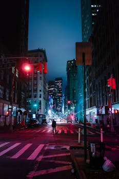 Dramatic city street at night with vibrant lights and tall buildings in a bustling urban setting.