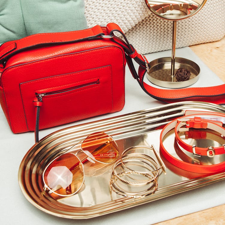 
A Red Leather Bag Beside A Tray Of Accessories