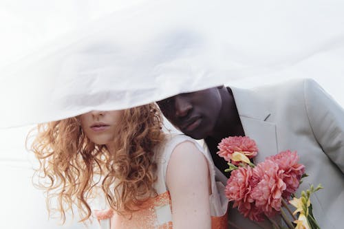 Young Fashionable Man and Woman Standing under Delicate White Fabric 