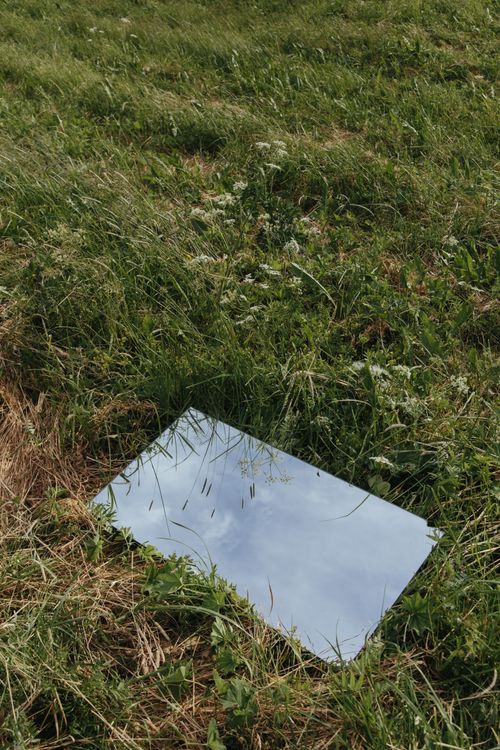 Free A mirror reflecting the sky placed on grassy field, showcasing nature's beauty. Stock Photo