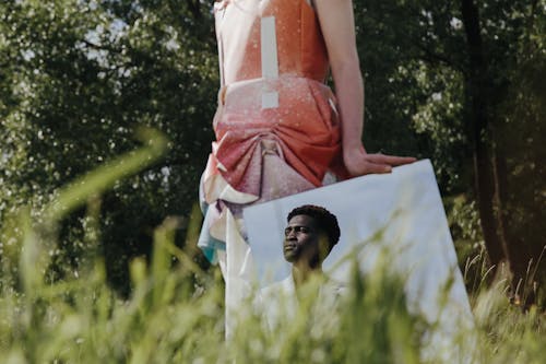 Reflection of a Man in a Suit in a Mirror Held by a Woman Standing on a Meadow 