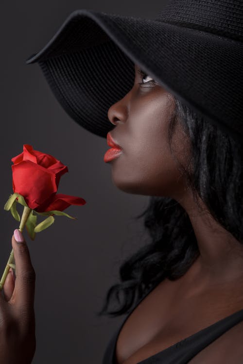 
A Woman Wearing a Hat Holding a Red Rose