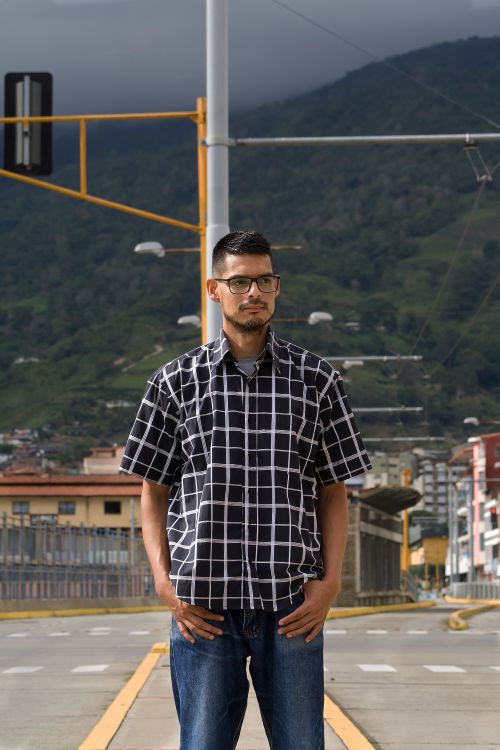 Free A man wearing a checkered shirt stands confidently outdoors in Venezuela with a scenic mountain backdrop. Stock Photo