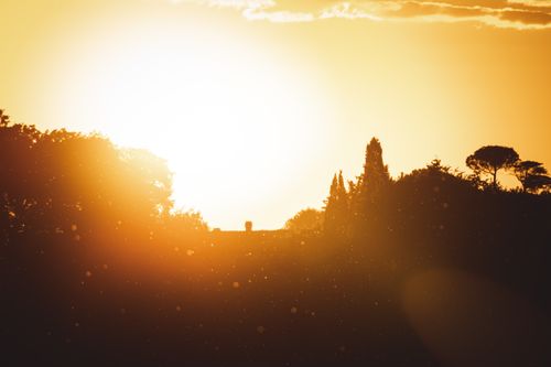Free Serene sunset casting silhouettes over hills and trees, creating a warm glow. Stock Photo