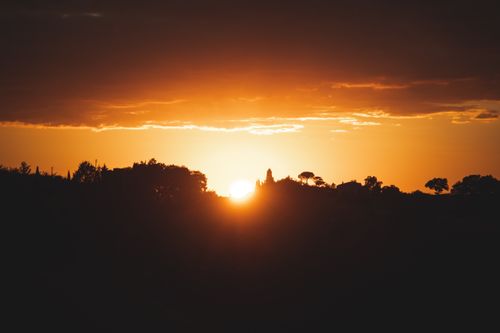 Free Beautiful sunset casting warm hues over a silhouetted landscape with dramatic sky. Stock Photo