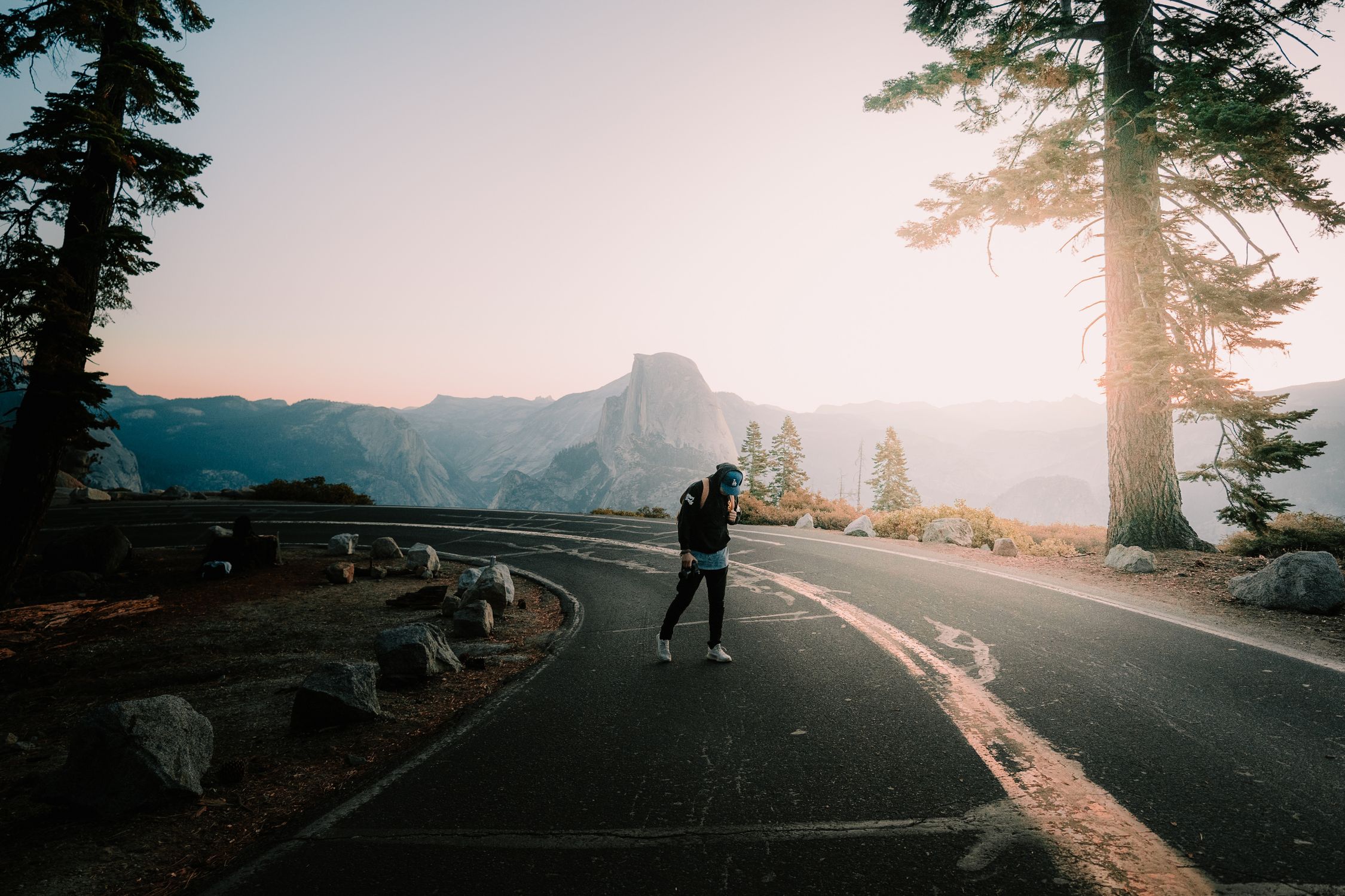A person walking on a winding road in Yosemite National Park at sunrise with Half Dome in the background.
