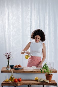 A young woman pours olive oil while preparing a meal with fresh ingredients in a rustic kitchen setting.