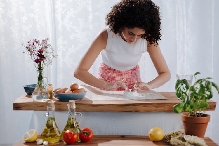 Young Woman Mixing Pasta Ingredients On Kitchen Table