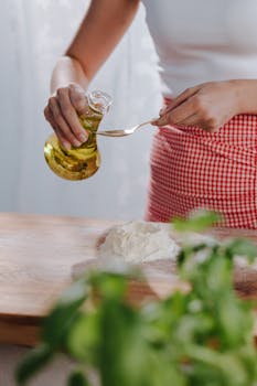 Woman pours olive oil onto flour on a wooden board, preparing homemade pasta.