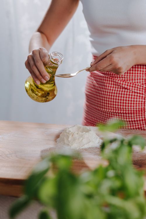 Free Woman pours olive oil onto flour on a wooden board, preparing homemade pasta. Stock Photo