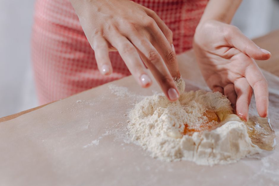Close-up of hands kneading dough with flour on a kitchen table, preparing homemade pasta.