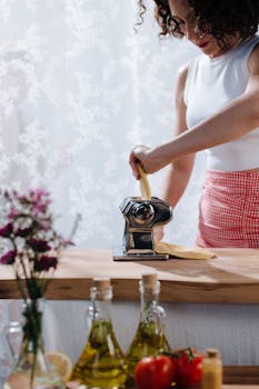 A woman using a pasta maker in a kitchen with fresh ingredients and vibrant setup.