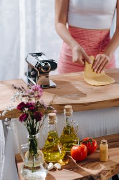 Close-up of a woman preparing fresh pasta dough with olive oil and tomatoes on a wooden table.