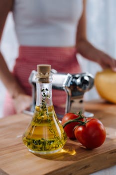 Close-up of olive oil, tomatoes, and pasta machine on a wooden board.
