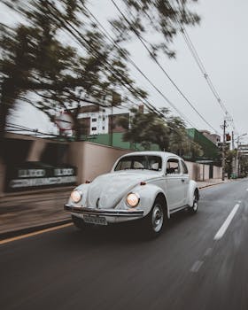 A classic white vintage car driving through the streets of Curitiba, Brazil on a cloudy day.