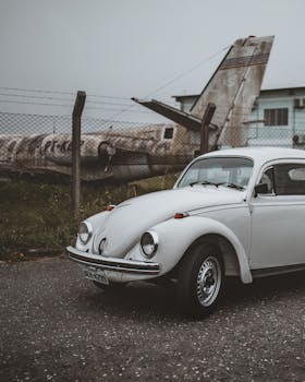 Classic white Volkswagen Beetle parked near an old airplane in Curitiba, Brazil.
