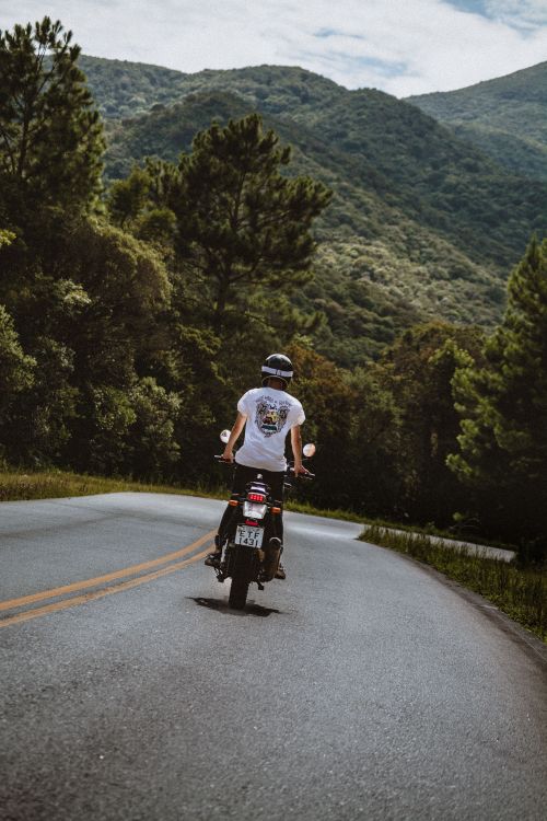 Free A motorcyclist enjoys a scenic ride on a winding road surrounded by lush green mountains and trees in Brazil. Stock Photo
