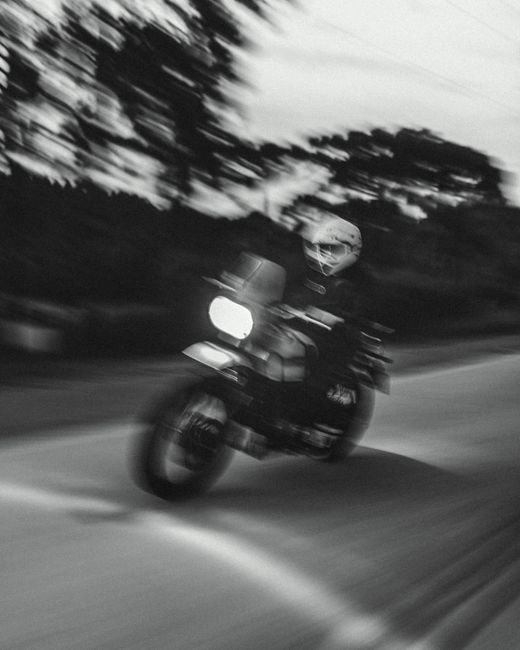 Dynamic black and white rolling shot of a motorcycle speeding on a curving road.