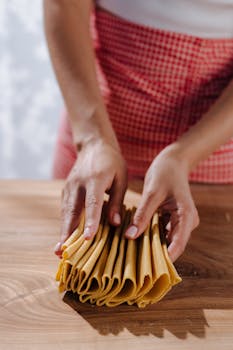 A person carefully arranging fresh uncooked pasta sheets on a wooden table.