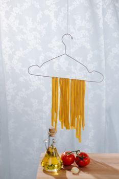 Unique presentation of pasta hanging on a hanger with tomatoes and oil.
