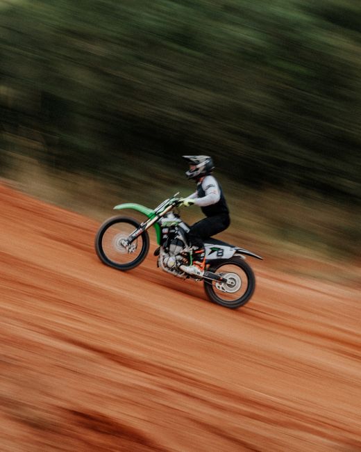 High-speed dirt bike action shot on a vibrant red dirt track in Curitiba, Brazil.