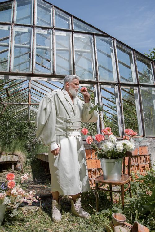 Free Elderly man with gray hair smelling vibrant flowers in a sunny greenhouse garden setting. Stock Photo