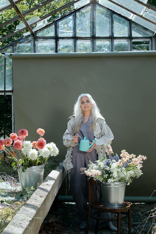 Elderly Woman Standing Near Flowers Holding Watering Can
