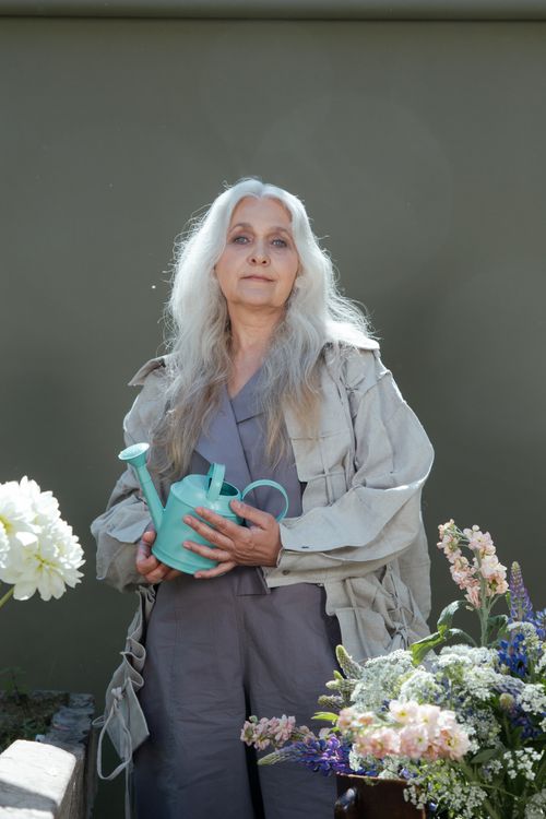 Free Senior woman with grey hair holding a teal watering can in a garden setting. Stock Photo