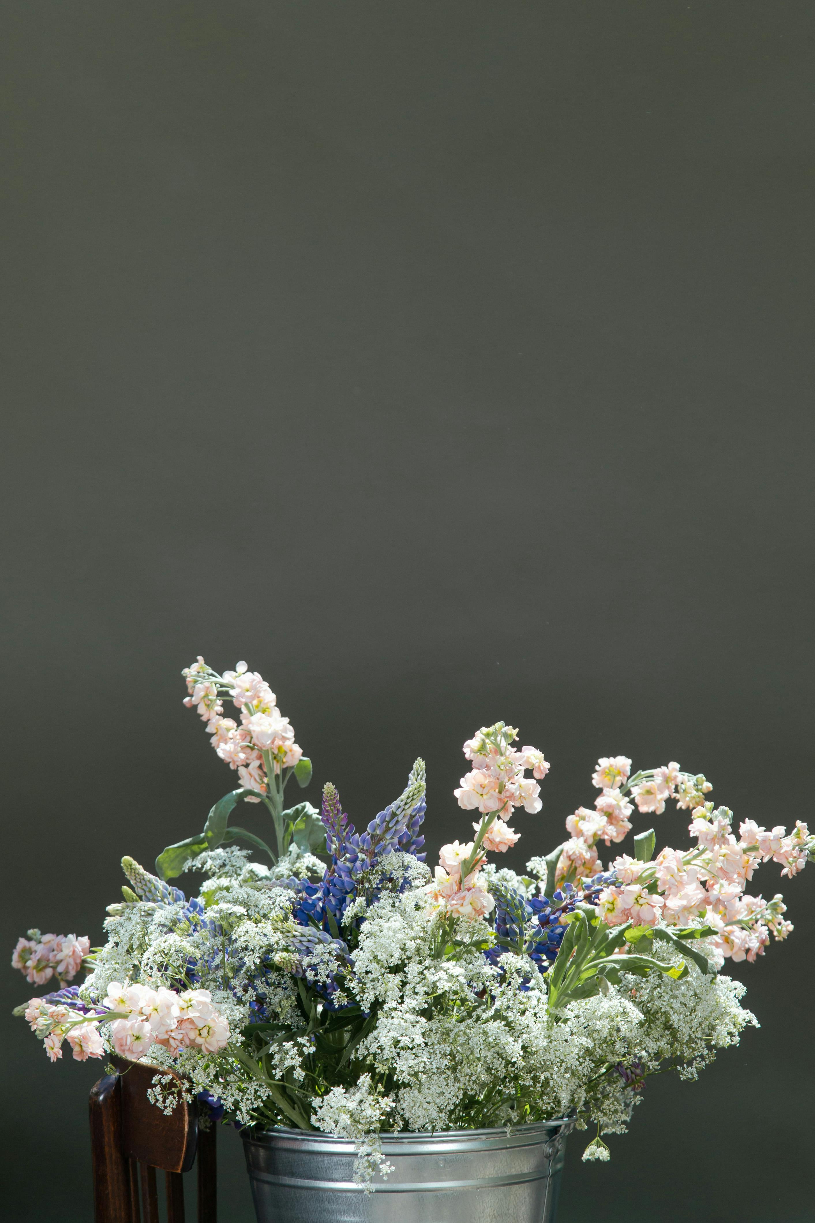Charming bouquet of wildflowers displayed in a rustic metal bucket against a solid green backdrop.