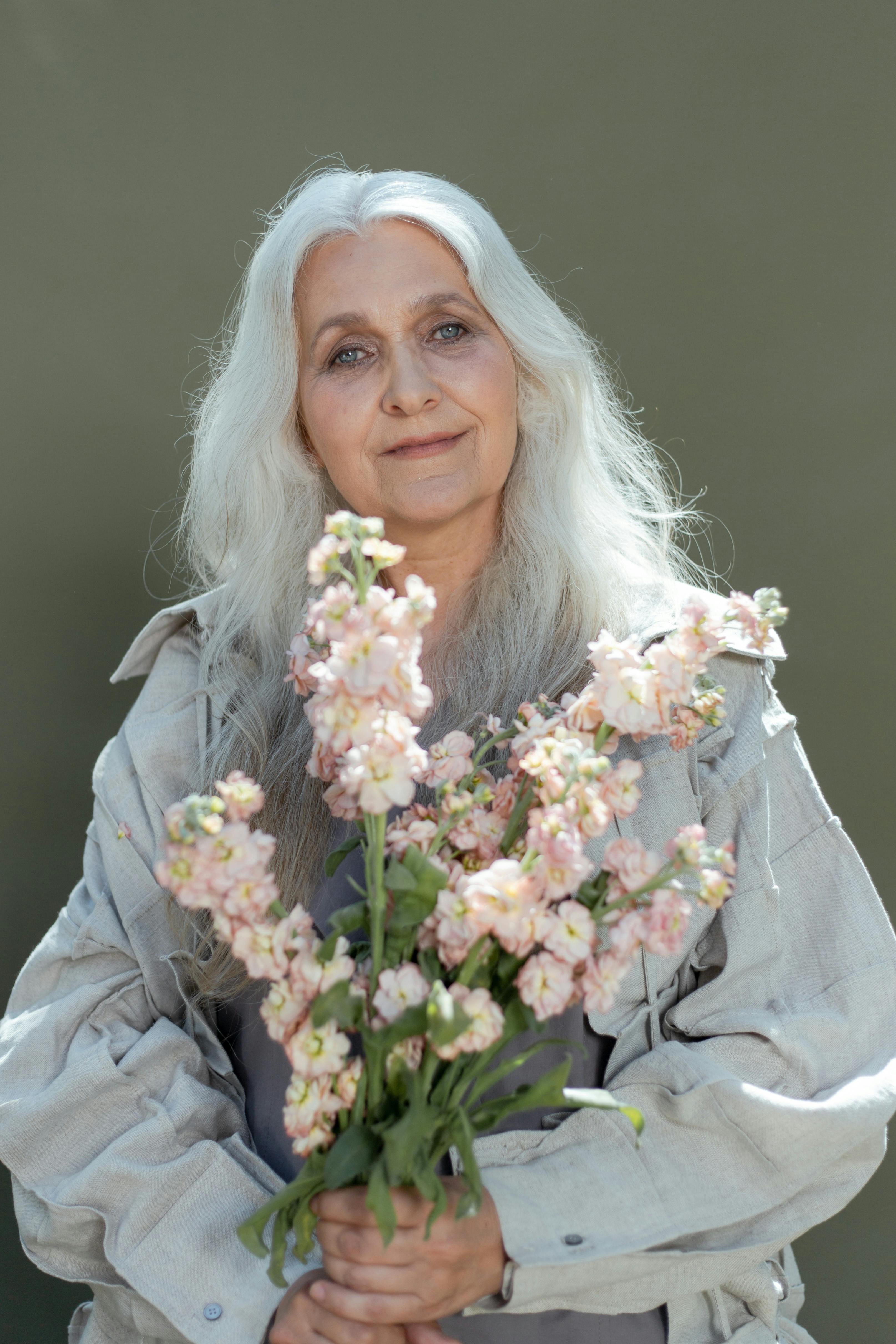 a mature woman wearing gray coat holding a bunch of flowers