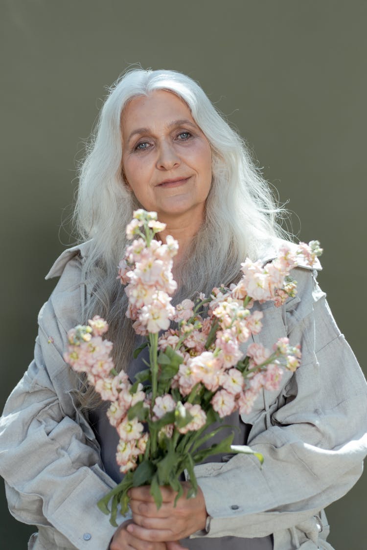 A Mature Woman Wearing Gray Coat Holding A Bunch Of Flowers