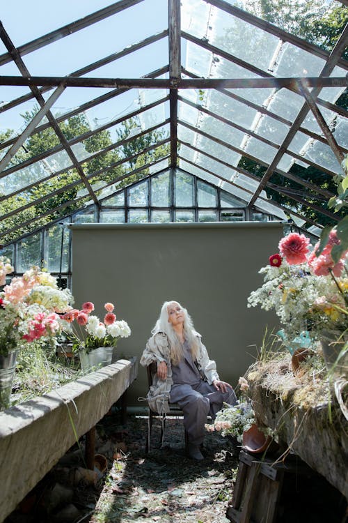 Photo of a Woman Sitting in an Abandoned Greenhouse with Flowers