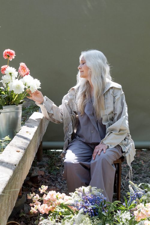 Free Elderly woman sitting peacefully surrounded by flowers in a greenhouse. Stock Photo