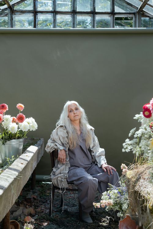 Free Elegant senior woman with gray hair sitting in a greenhouse surrounded by vibrant flowers. Stock Photo