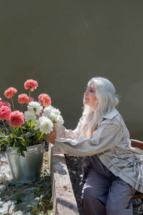 Free A senior woman with long gray hair tenderly attending to garden flowers in a peaceful setting. Stock Photo