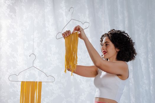 Woman uses clothes hangers to dry handmade pasta indoors, embracing Italian cooking tradition.