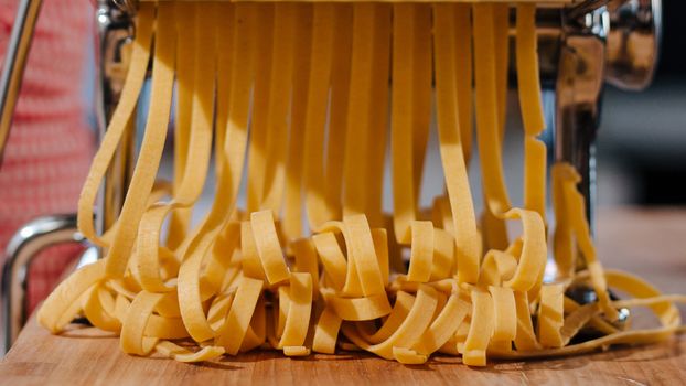 Close-up of fresh pasta strands being made with a pasta machine in an indoor kitchen setting.