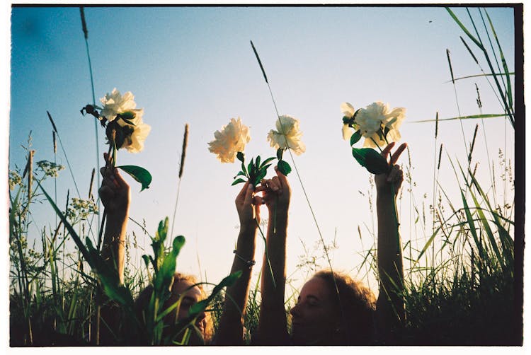 Photograph Of Girls Holding Flowers High In Hands