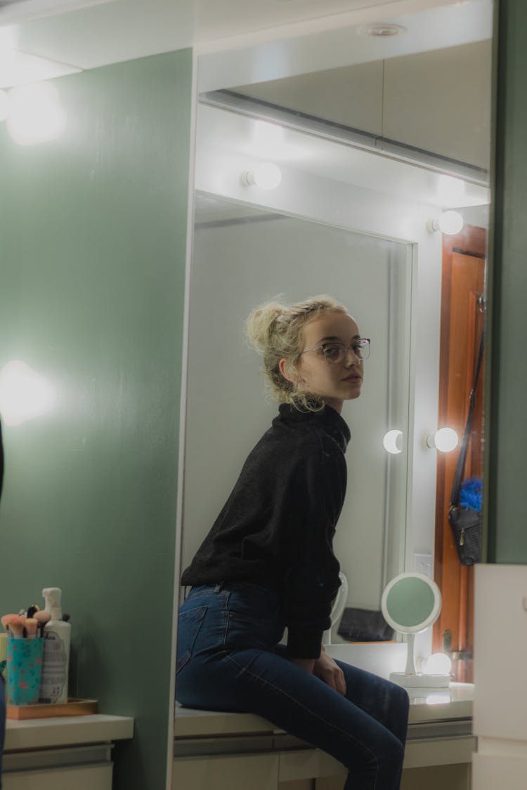 A Woman Sitting On A Dresser Mirror Table