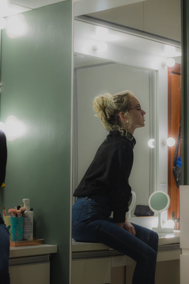 

A Woman Wearing A Black Sweater And Denim Pants Sitting On A Table